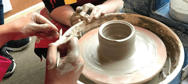 Image of hands working with clay on a pottery wheel.