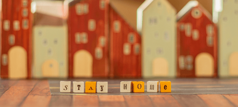 "Stay home" written in cube letters. Blurred outlines of miniature buildings can be seen in the background.