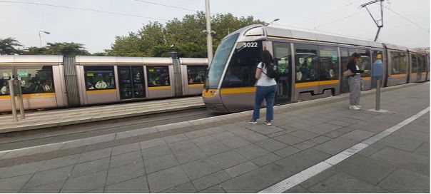 A photograph of a tram stop with one tram at the back and one drawing into the stop